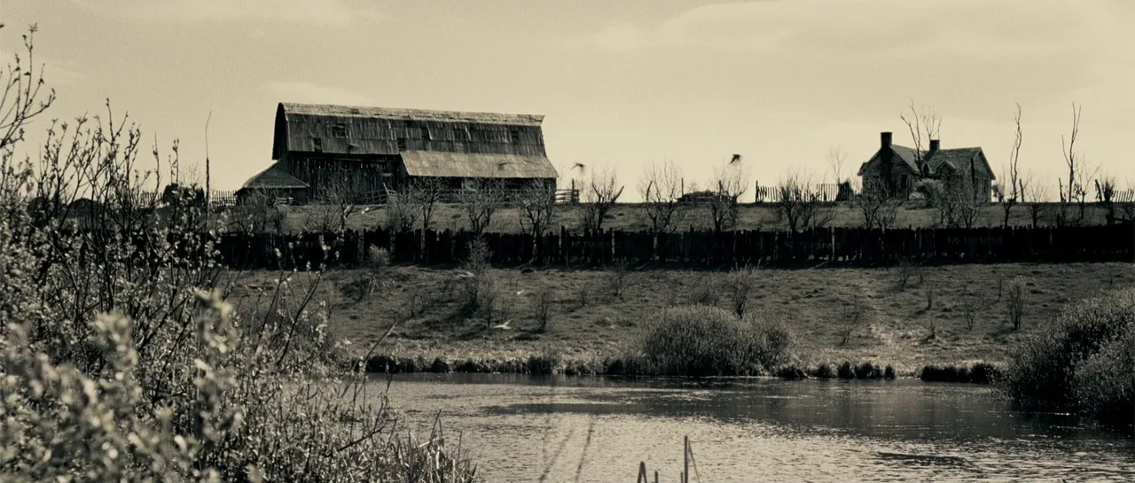 Blood Creek (2009) movie still: establishing — A rural landscape features a weathered barn and a house atop a gentle hill. A wooden fence separates…
