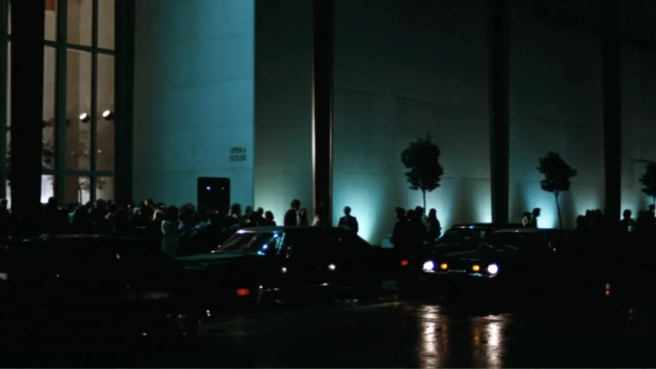 All the President's Men (1976) movie still: wide — A modern building exterior at night features a crowd gathering near parked automobiles. Tall…