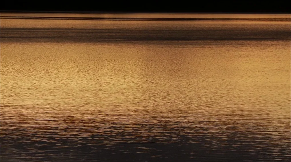 Your Sister’s Sister (2011) movie still: establishing — A vast expanse of water ripples under the light of the setting sun. The surface reflects…