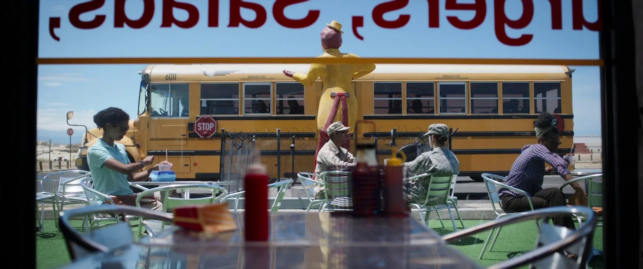 The Mauritanian (2021) movie still: wide — An outdoor dining area features metal furniture on a green synthetic grass surface. A bright yellow…