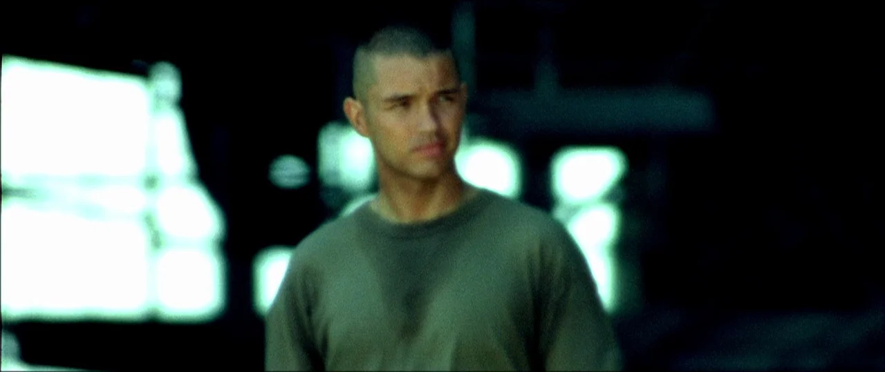 Black Hawk Down (2001) movie still: medium — A man stands in an outdoor area at night with blurred industrial lights behind him. The figure is…