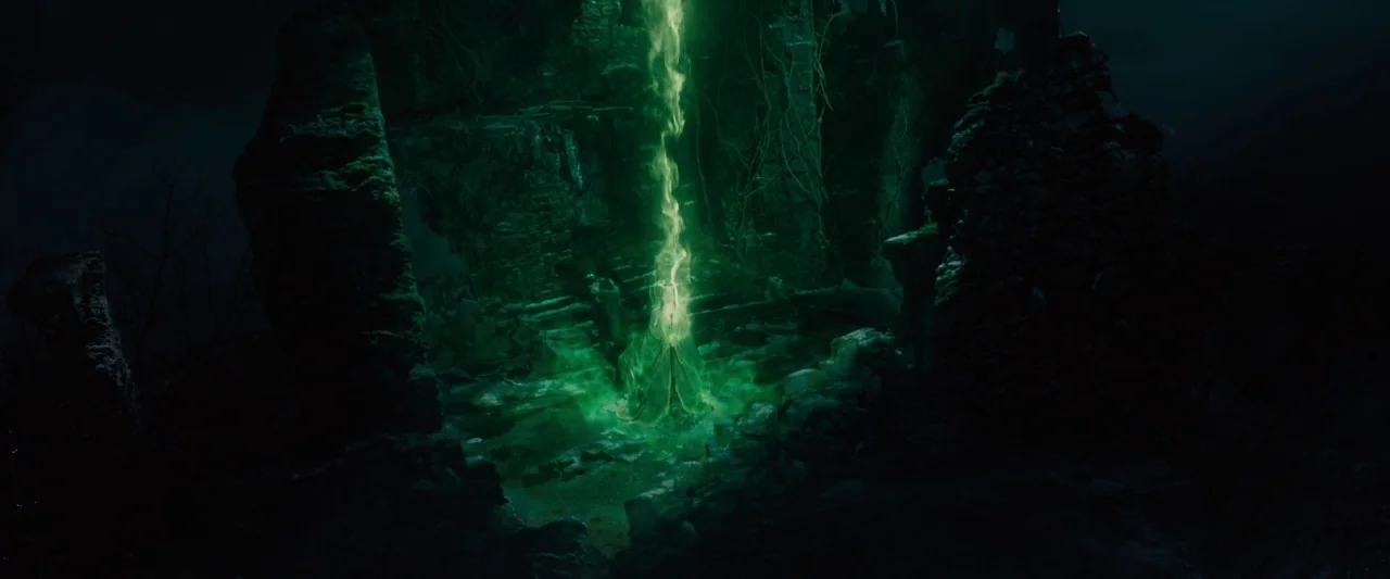 Maleficent (2014) movie still: establishing — Dark stone ruins stand in the middle of a dim, overgrown landscape. A vertical column of radiant green…