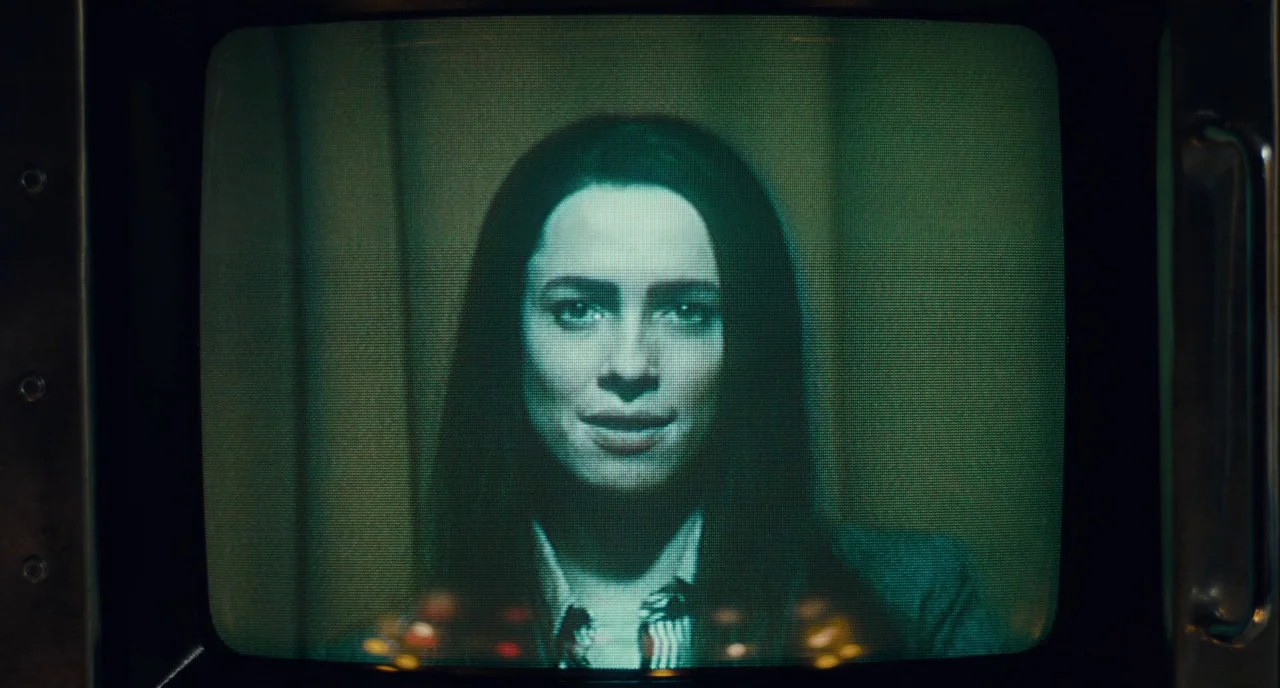Christine (2016) movie still: closeup — A woman's face appears within the rectangular frame of an old-fashioned analog television set. The screen…
