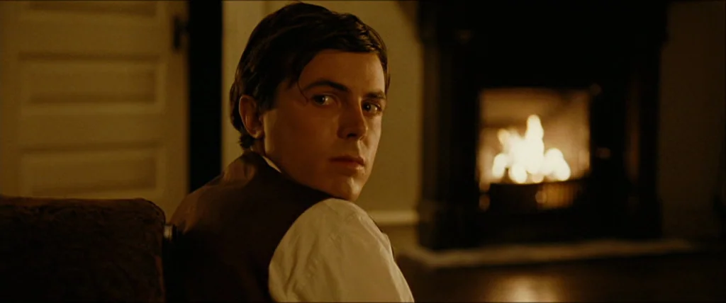 The Assassination Of Jesse James By The Coward Robert Ford (2007) movie still: medium — A dimly lit room features a burning fireplace hearth against…