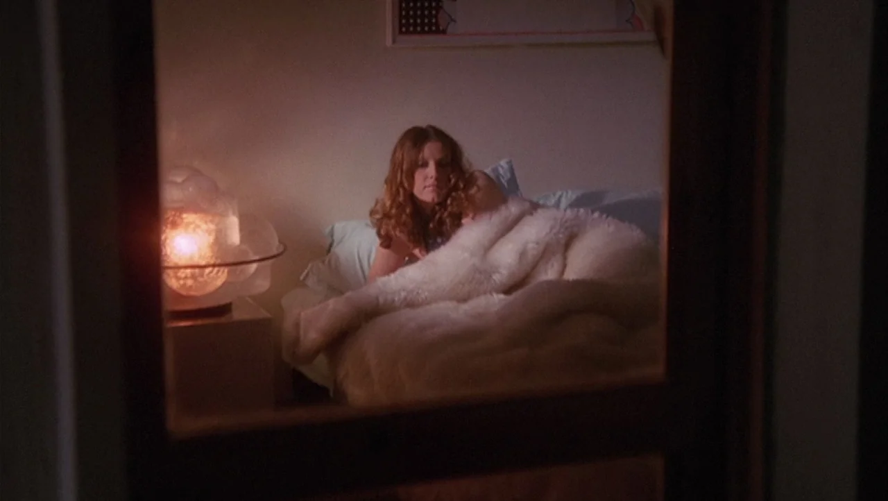The Black Belly of the Tarantula (1971) movie still: medium — A woman rests in bed illuminated by the orange glow of a bedside glass lamp. She is…