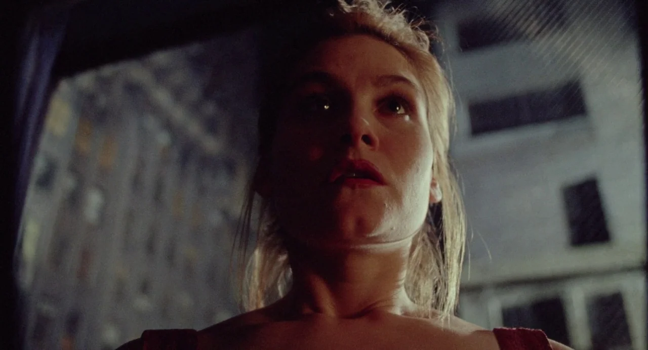 What Happened Was… (1994) movie still: closeup — A woman stands indoors at night looking through an open window at city buildings. She gazes outward…