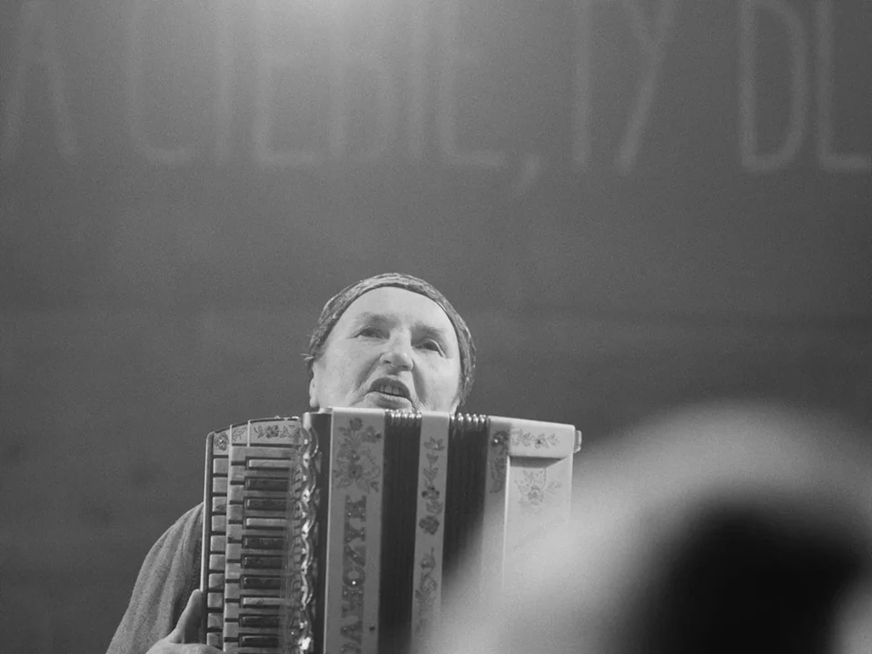 Cold War (2018) movie still: closeup — A woman stands on a stage performing with a floral-painted accordion. A blurred object is in the lower right…