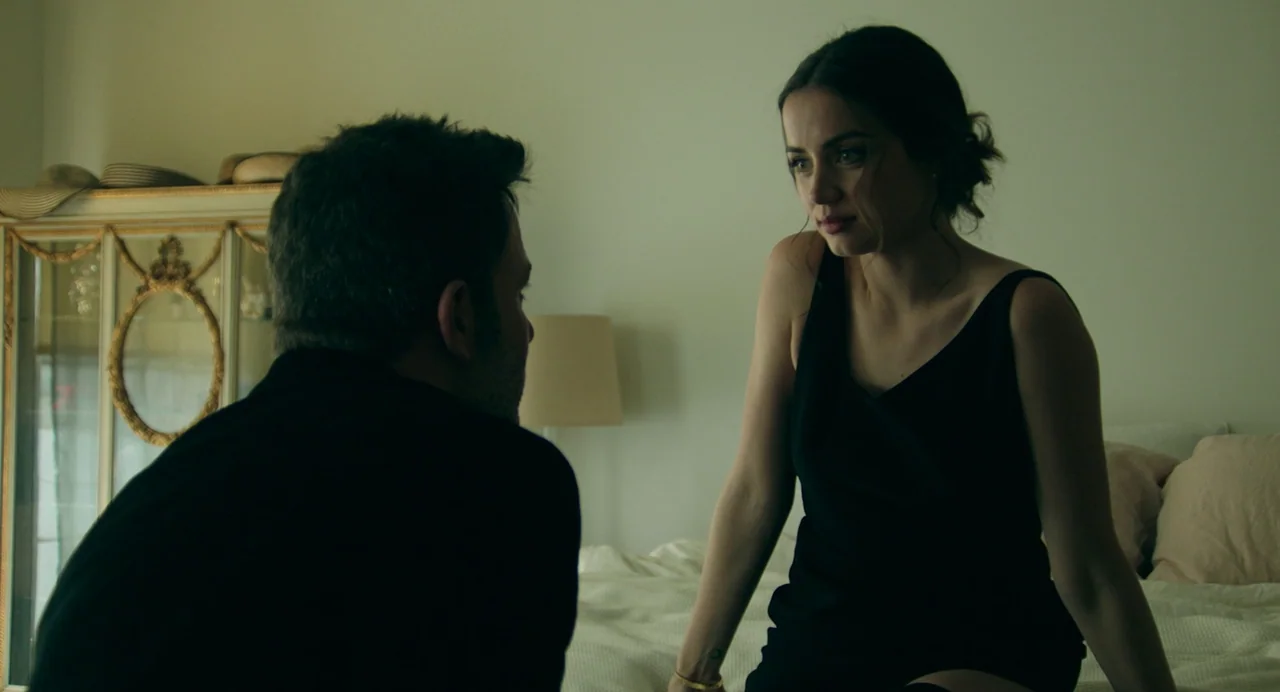 Deep Water (2022) movie still: medium — An interior bedroom space with a light-colored headboard and a decorative display cabinet behind. A woman…
