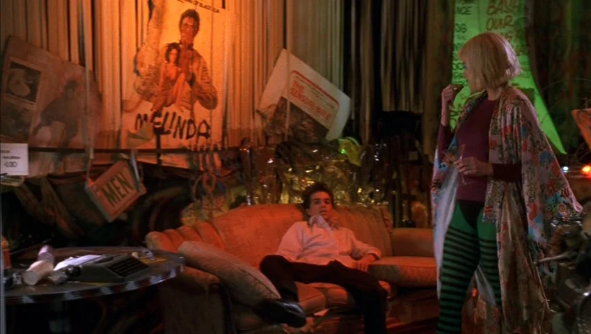 Making of: Castle Freak (1995) movie still: medium — A cluttered apartment interior filled with posters and miscellaneous objects on the walls. A…