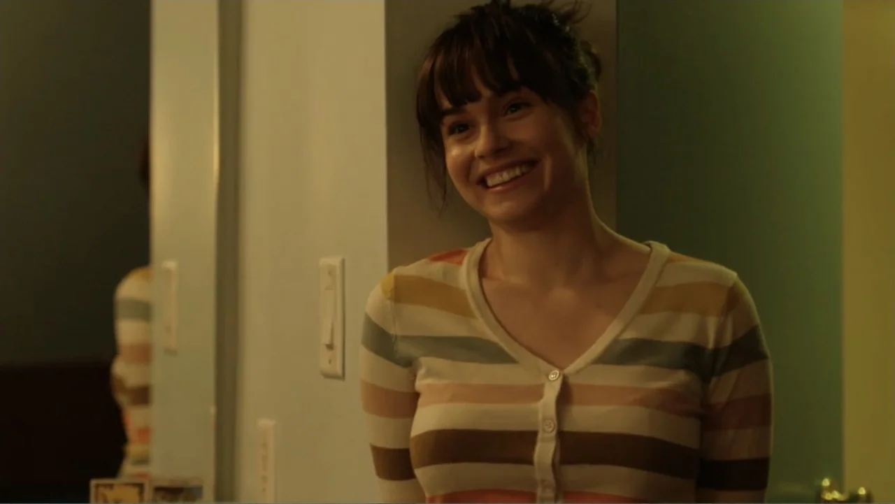 Like.Share.Follow. (2017) movie still: medium — A woman stands in a dimly lit domestic hallway near a light switch. She smiles toward the camera…