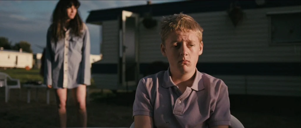 The Scouting Book for Boys (2009) movie still: medium — A field filled with mobile homes serves as a backdrop at golden hour. A young boy sits in…