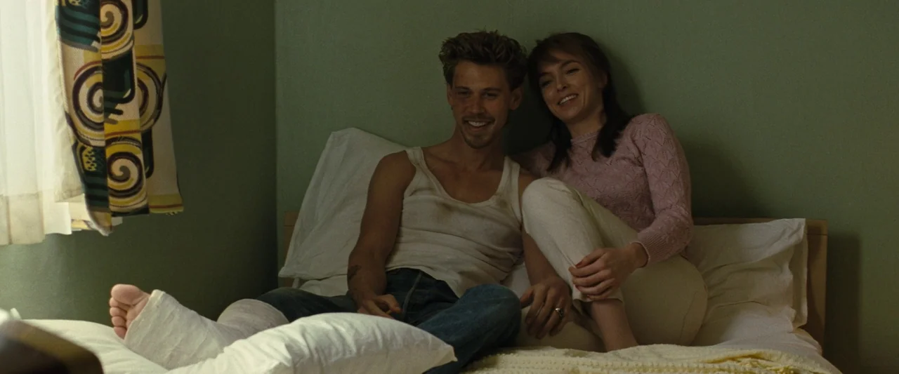 The Bikeriders (2023) movie still: medium — A modest room features plain green walls and a single bed with white linens. A man with a leg cast and a…