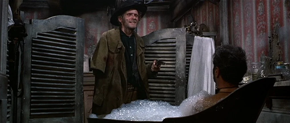 The Good, The Bad And The Ugly (1966) movie still: medium — A dimly lit, vintage bathroom features faded patterned wallpaper and wooden louvered…