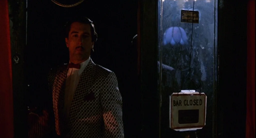 The King Of Comedy (1982) movie still: medium — A dimly lit room with a dark entrance and a hanging 'Bar Closed' sign. A man in a patterned suit…