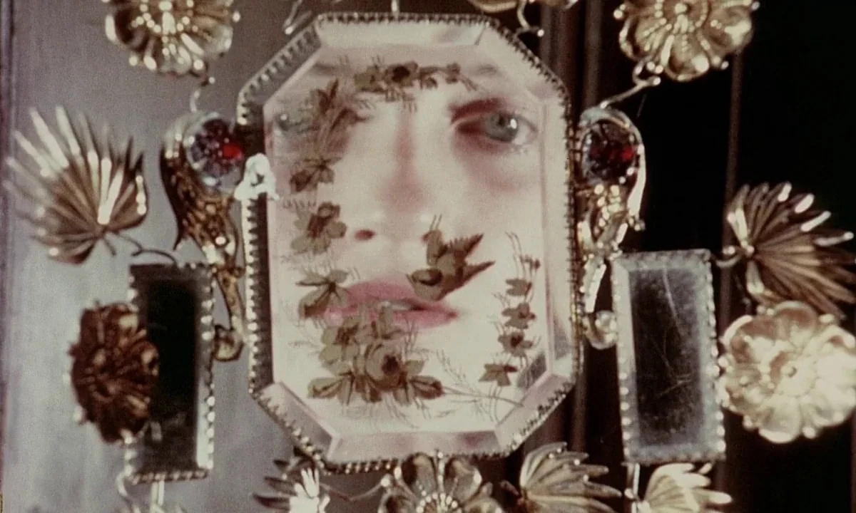 Immoral Tales (1974) movie still: closeup — An ornate gold mirror with intricate floral and avian metalwork sits in a room. The reflection shows the…