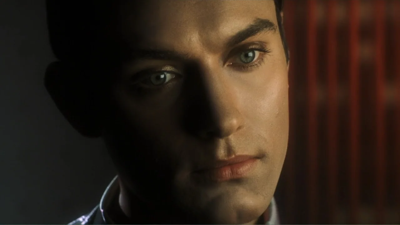 A.I. Artificial Intelligence (2001) movie still: closeup — A man's face is illuminated in a dark interior space with vertical lines in the…