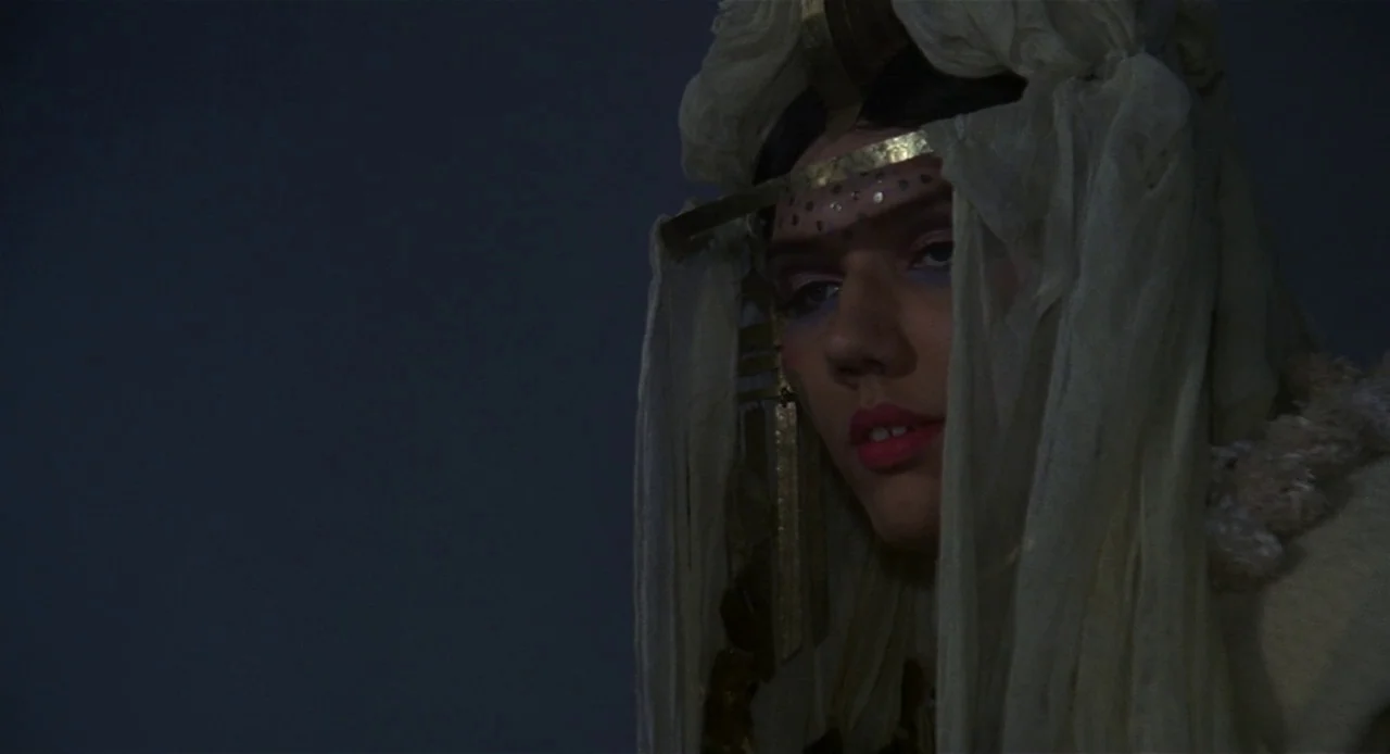 Fellini’s Casanova (1976) movie still: closeup — A person stands in darkness wearing a complex white and gold headpiece. The subject faces the…