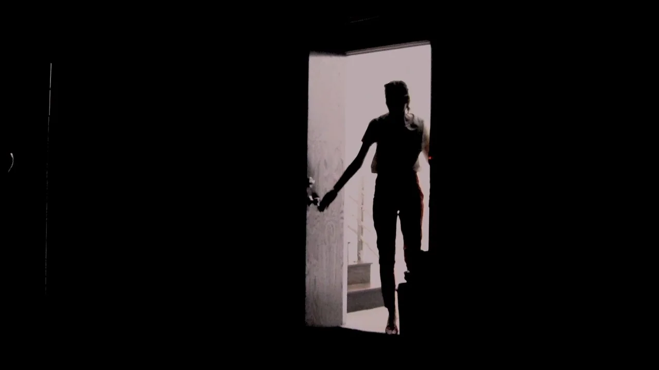 The ABCs of Death (2012) movie still: fullbody — A dark space frames a bright rectangular opening showing an adjacent exterior area. A silhouette of…