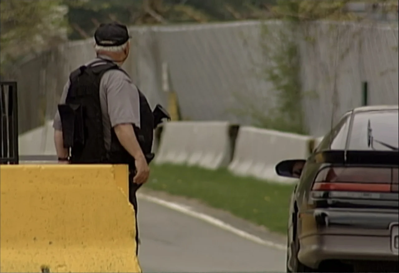 Indian Point: Imagining the Unimaginable (2004) movie still: medium — An outdoor security checkpoint features concrete barriers and a chain link…