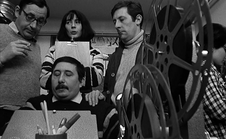 Who Are You, Polly Maggoo? (1966) movie still: medium — A workspace cluttered with film equipment includes a large metal film reel in focus. Four…