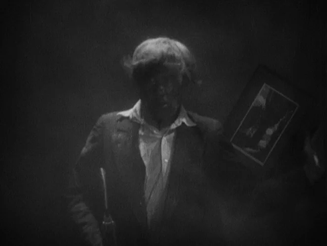 Underworld (1927) movie still: medium — A dark, indistinct room filled with smoke or fog that obscures the background. A man in a suit stands in the…
