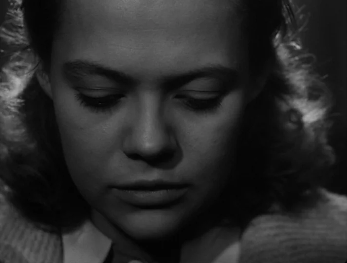 Port of Call (1948) movie still: closeup — A dark, undefined interior space serves as the background for a close portrait. A woman's face is…