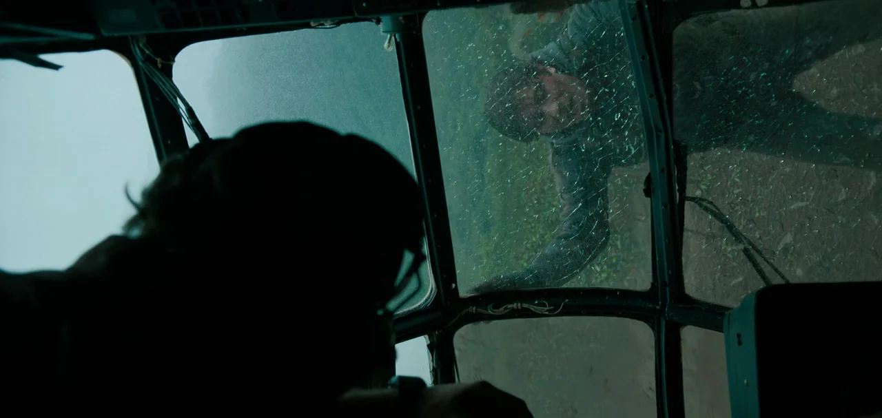 Triple Frontier (2019) movie still: medium — A view from inside a helicopter cockpit looking through a cracked window pane. A man stands outside on…