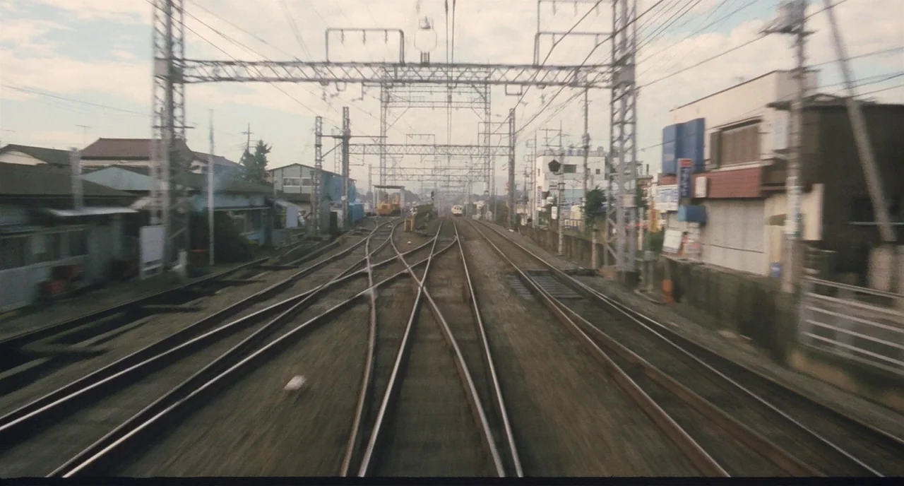 Tampopo (1985) movie still: establishing — A complex network of converging railway tracks cuts through a suburban residential area. Overhead wires…