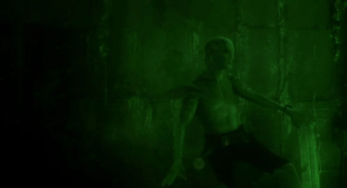 Hellboy (2004) movie still: medium — A murky underwater environment with dark, textured vertical surfaces in the background. A lean humanoid figure…