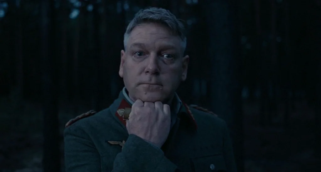Valkyrie (2008) movie still: medium — A man in a German military uniform stands in a dark forest at night. He is centered in the frame with his hand…