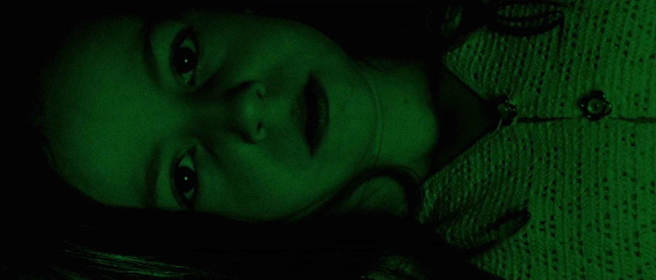 Amer (2009) movie still: closeup — The interior of a vehicle is bathed in saturated green light at night. A young woman with dark hair lies down…