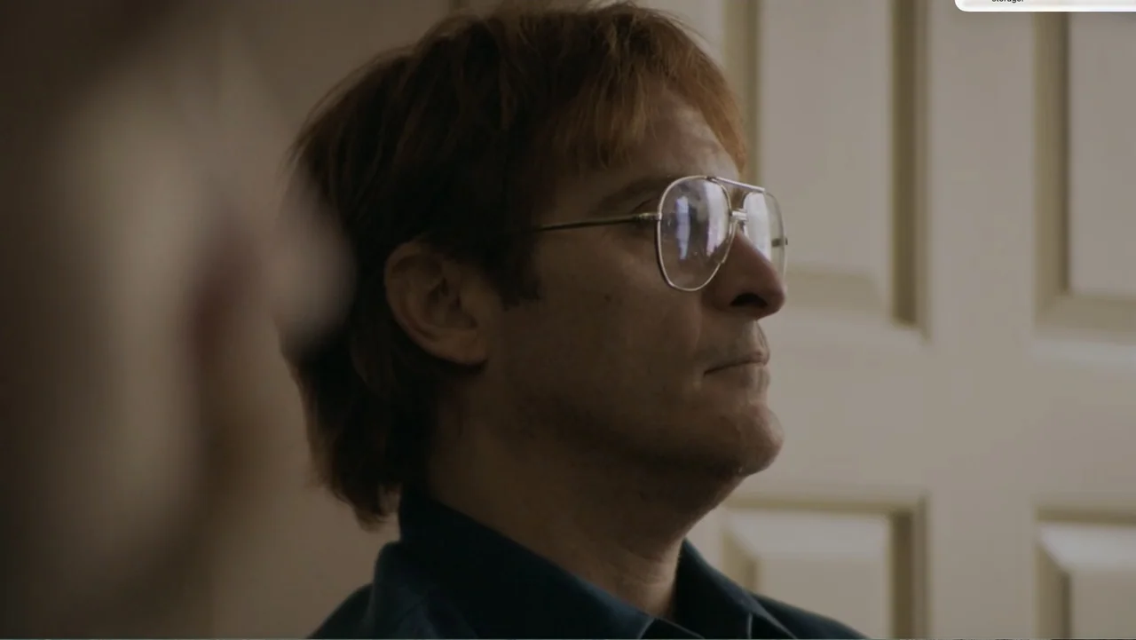 Don't Worry, He Won't Get Far on Foot (2018) movie still: closeup — A quiet indoor office space with a paneled door visible in the background. A man…