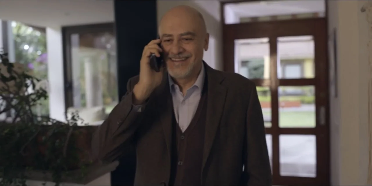 El sabor de la Navidad (2023) movie still: medium — A well-lit residential hallway features a glass door leading to a garden outside. A middle-aged…