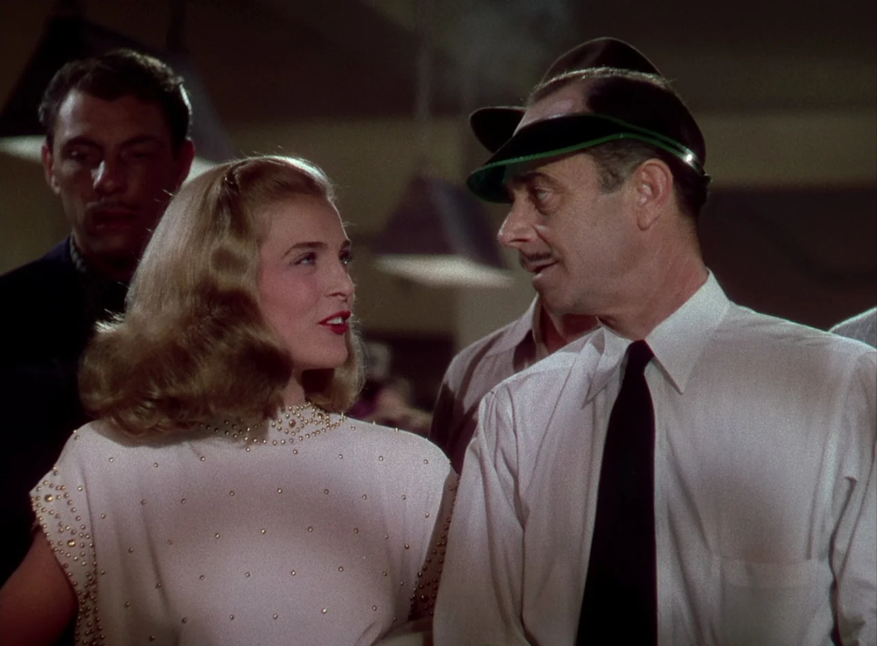 Desert Fury (1947) movie still: medium — A dimly lit room with blurred architectural details in the background. A woman in a beaded top talks to a…