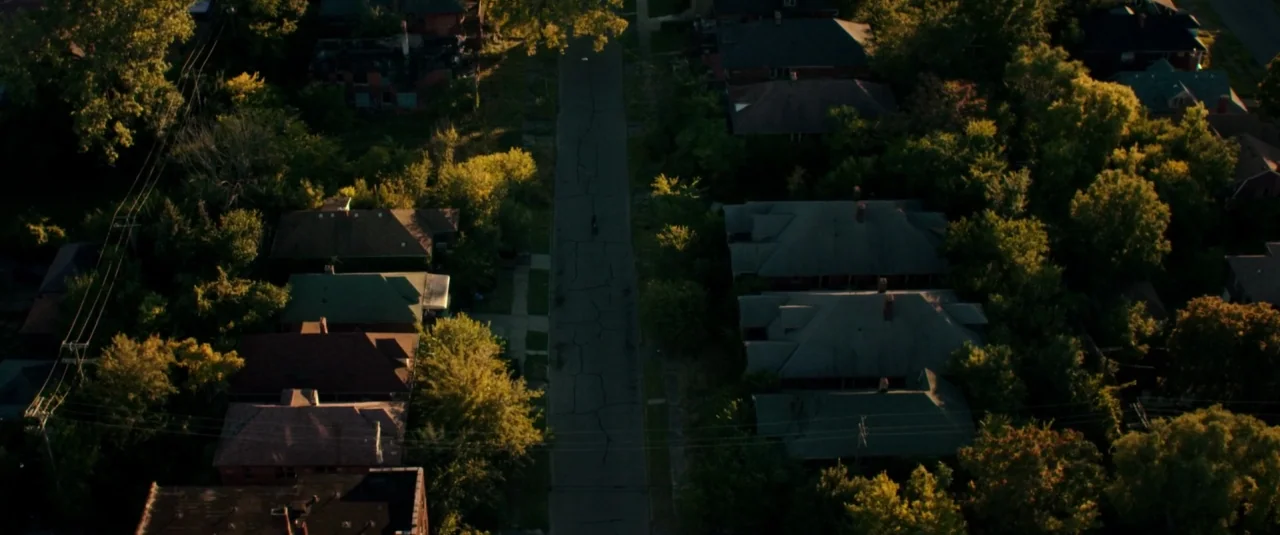 Don’t Breathe (2016) movie still: establishing — An overhead view of a narrow, cracked residential street flanked by old houses and trees. Dense…