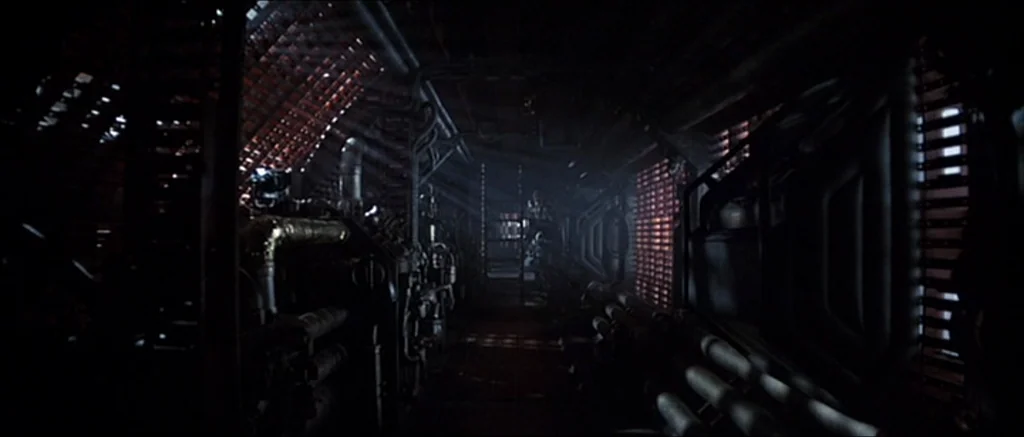Alien (1979) movie still: establishing — A dimly lit, narrow industrial corridor on a spaceship features exposed pipes and metal machinery.…