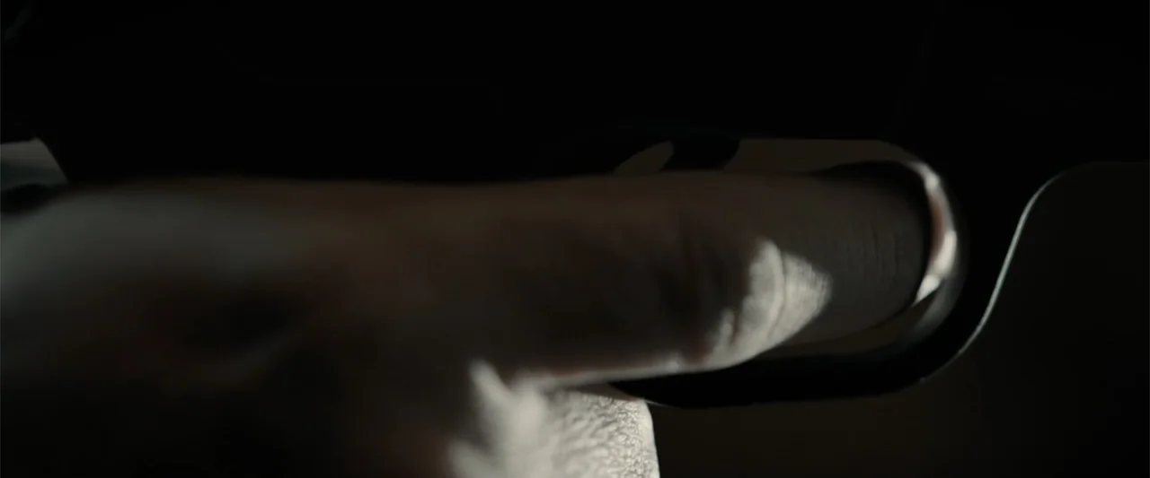 The Equalizer 3 (2023) movie still: closeup — A dark interior setting shows a macro view of a firearm mechanism. A finger is positioned against the…