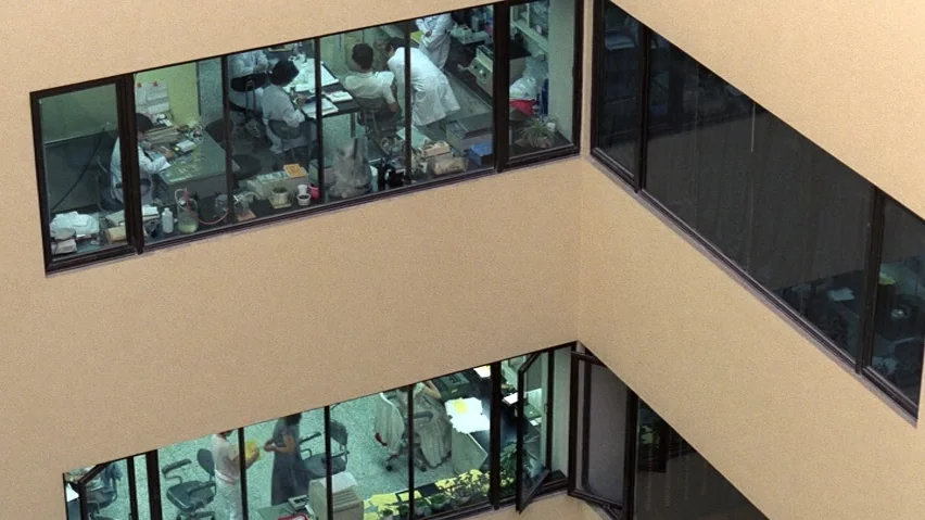 The Terrorizers (1986) movie still: wide — A high-angle view shows two floors of a modern building with large glass windows. People wearing white…