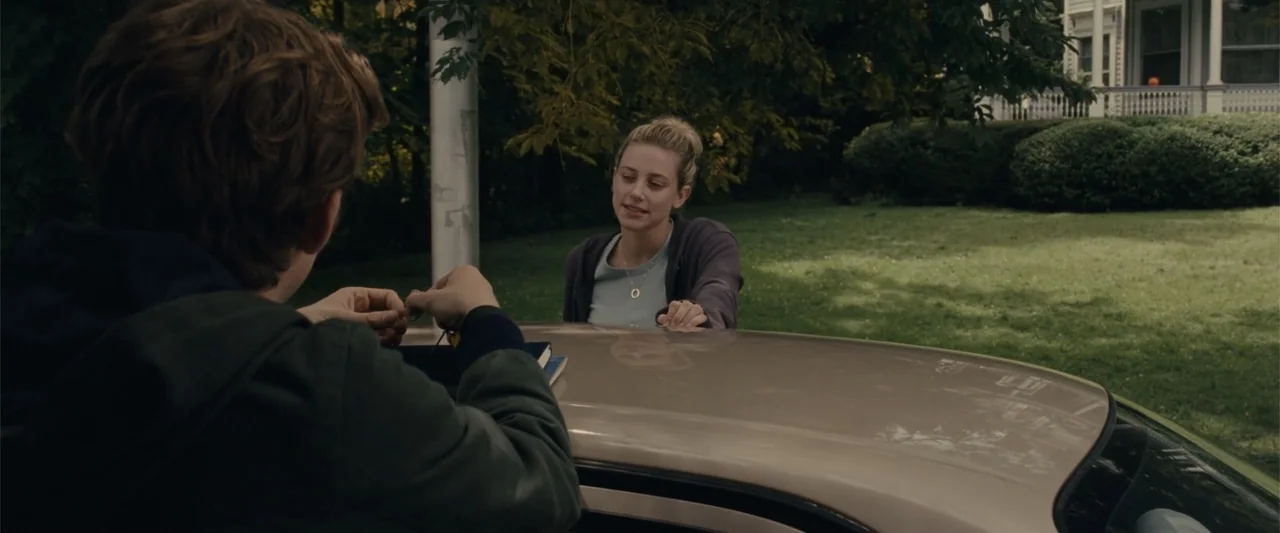 Chemical Hearts (2020) movie still: medium — A residential driveway with a green lawn and a distant house in view. A young man facing away holds…