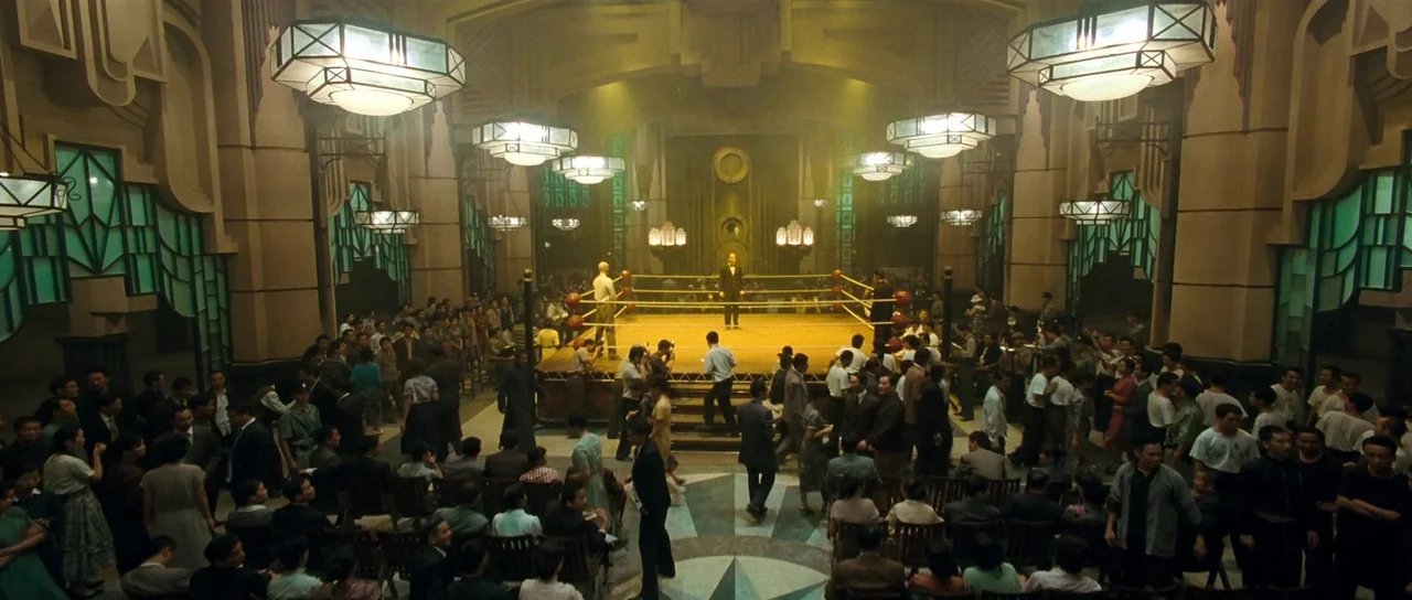 Ip Man 2 (2010) movie still: wide — A high-ceilinged hall features art deco architecture and large hanging geometric lights above a central boxing…