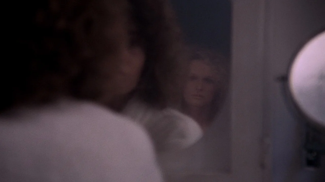Fatal Attraction (1987) movie still: closeup — A dimly lit room with a mirror reflecting a woman's face. The subject watches her own reflection…