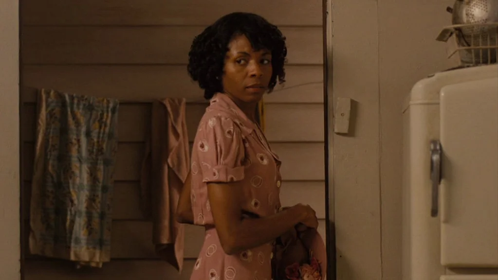 Honeydripper (2007) movie still: medium — A domestic space with wooden walls and a vintage refrigerator in the background. A woman in a pink dress…