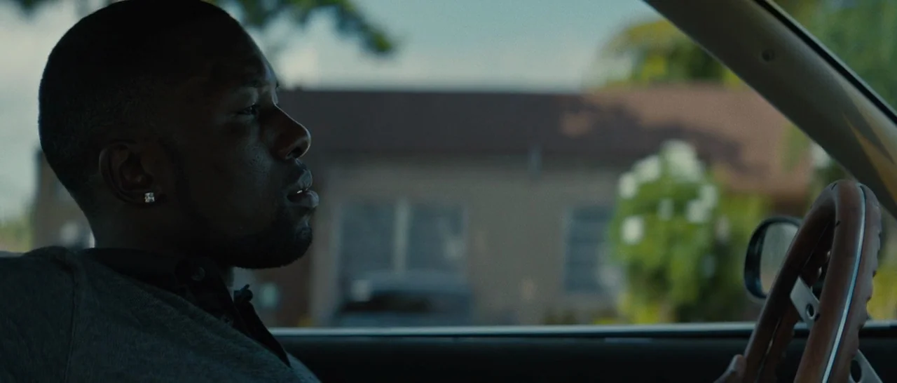 Moonlight (2016) movie still: medium — A man drives a car through a residential suburban neighborhood during the day. He sits behind the steering…