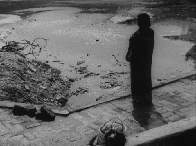 Drunken Angel (1948) movie still: wide — An industrial waterfront area with a stagnant pool of water filled with scattered debris. A lone elderly…