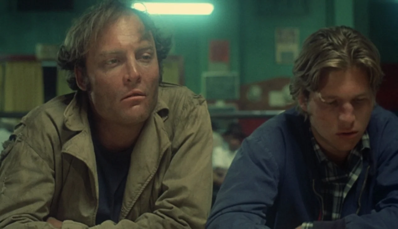 Fat City (1972) movie still: medium — A dimly lit room with green-tinted lighting features muted walls and worn furniture. Two men sit at a table…