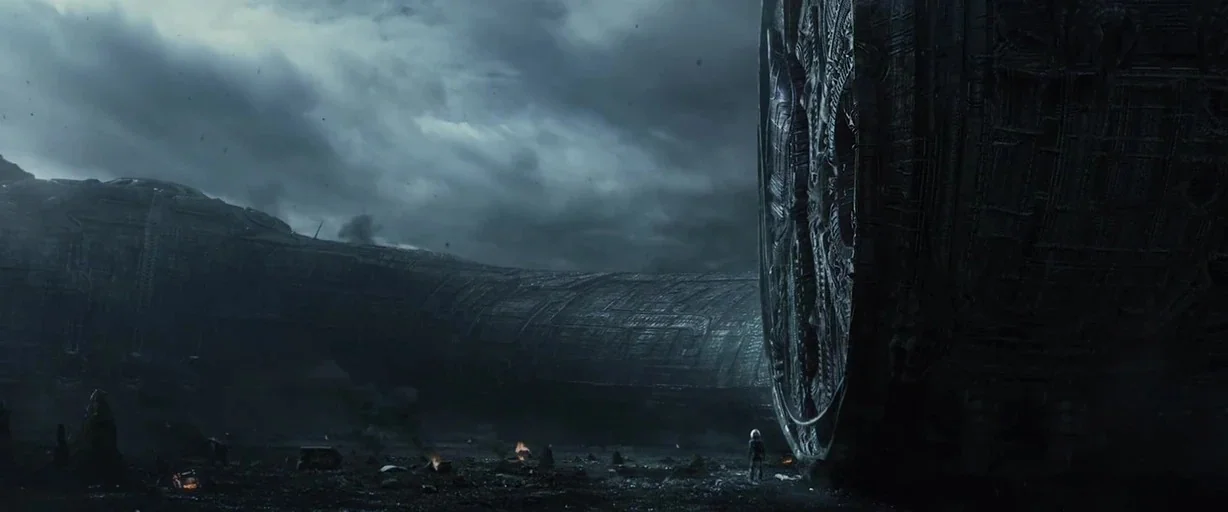 Prometheus (2012) movie still: establishing — A dark, rocky alien terrain features a massive, cylindrical, ornately textured structure stretching…