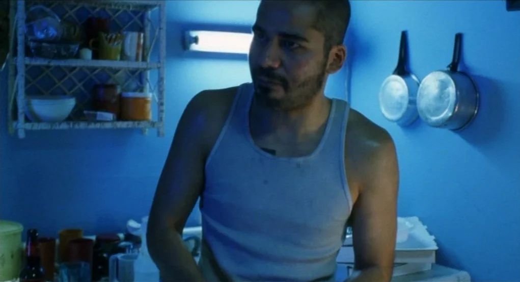 Narc (2002) movie still: medium — A small blue-walled living space is decorated with simple storage shelves and hanging cookware. A man in a white…
