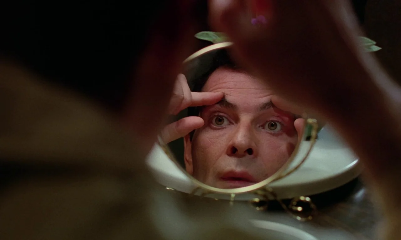 Rabid (1977) movie still: closeup — A close-up view through a small circular mirror reflects the face of a man. The man stares directly into the…