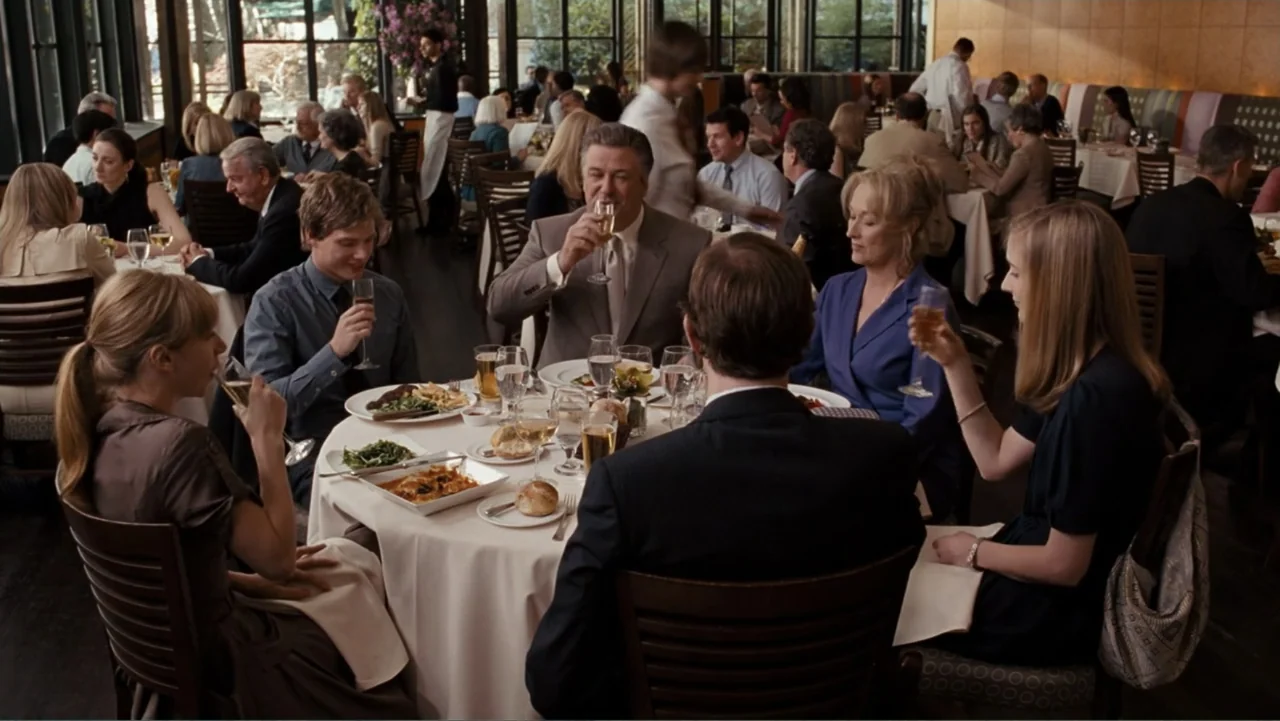 It's Complicated (2009) movie still: medium — A busy restaurant interior filled with various diners and wooden chairs at tables. Five adults sit…
