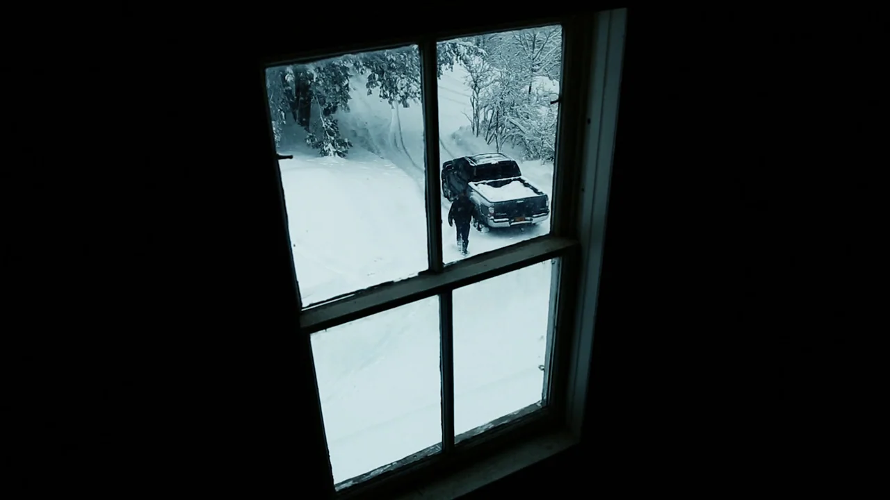 The Deeper You Dig (2019) movie still: wide — A dark indoor space looks out through a four-pane window into a snow-covered yard. A single…